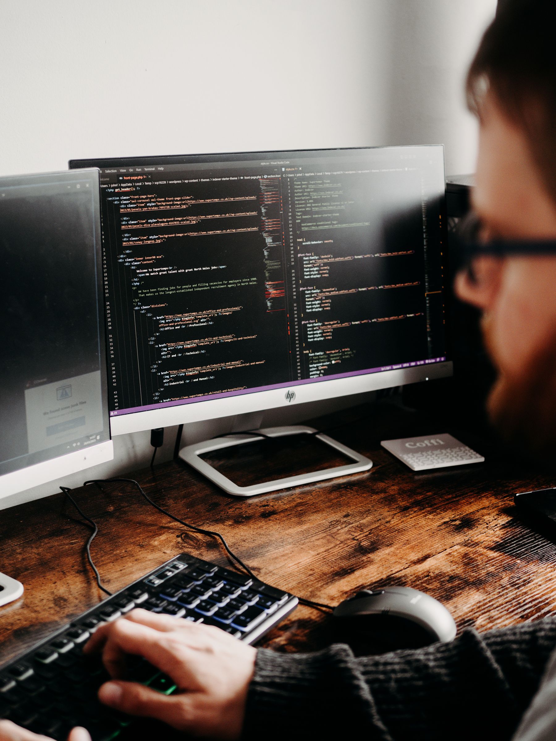 A software developer working with code across two monitors